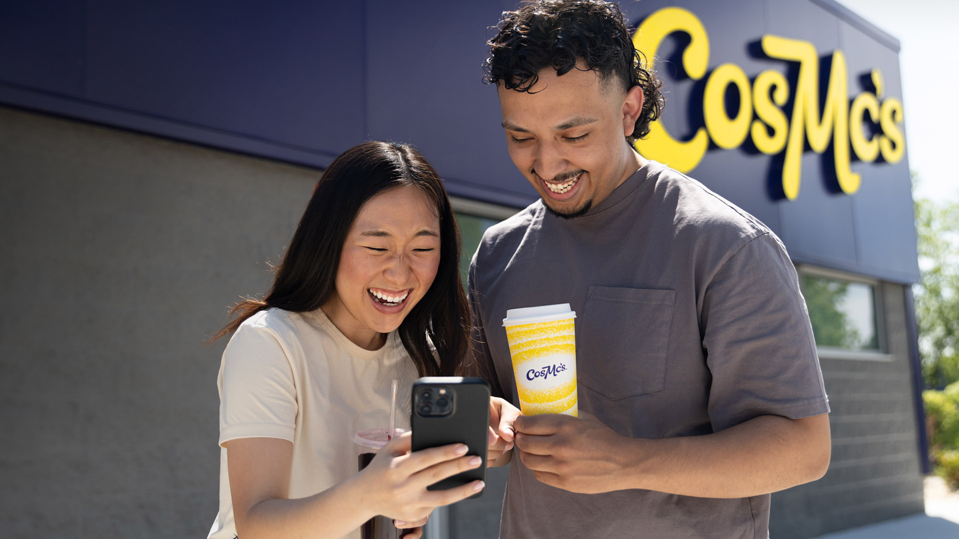 Two Zen Z people place an order on a mobile device in front of a CosMc's store.